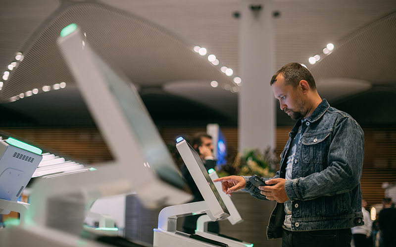 A male passenger at the electronic check-in desk in the departure area of the modern airport terminal. A young guy checks in for a plane at the screen of a self-service computer kiosk to check in for flights