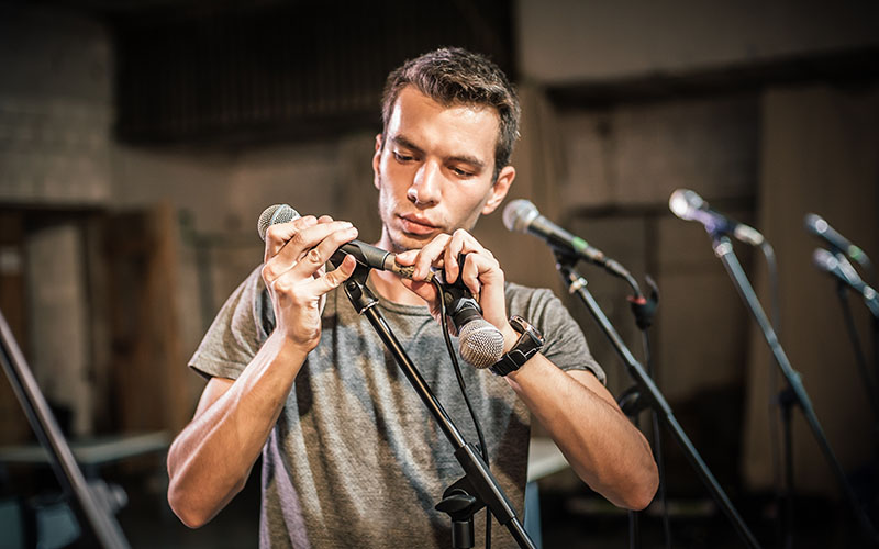 Theater audio technician adjusting an microphones on the scene. Installing and testing the sound system in the background
