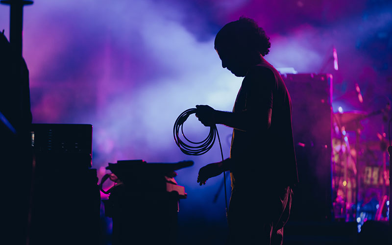 Silhouette of a stage worker on a stage holding the cables and setting up the lights for a music performance